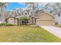 Tan house with palm trees, landscaped lawn, and two-car garage at 34 Black Creek Way, Ormond Beach, FL 32174