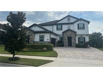 A charming two-story home with a stone facade, lush landscaping, and a paved driveway at 6301 Swanson St, Windermere, FL 34786