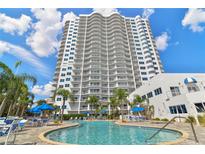 Luxury condominium building featuring a sparkling pool, palm trees, and blue umbrellas for relaxing by the water at 2 Oceans West Blvd # 1905, Daytona Beach Shores, FL 32118