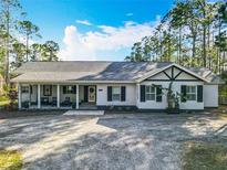 Charming single-story home featuring a covered porch, black shutters, neutral stucco, and mature trees at 4252 Quail Ranch Rd, New Smyrna Beach, FL 32168