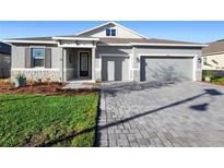 Charming single-story home featuring a stone facade, gray exterior, paver driveway, and well-manicured lawn at 875 Honey Petal Ln, Deland, FL 32720