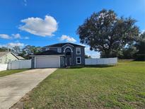 Two-story gray home featuring an arched entryway, attached garage, and a spacious green lawn under a bright blue sky at 2235 Rabenton Rd, Deltona, FL 32738