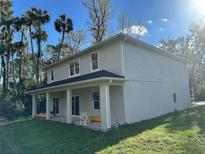 Two-story home with a covered porch and green lawn, surrounded by trees under a sunny blue sky at 283 Wildwood Dr, New Smyrna Beach, FL 32168