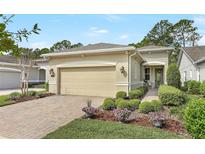 Charming home featuring a beige stucco exterior, brick driveway, manicured landscaping, and a two-car garage at 1684 Victoria Gardens Dr, Deland, FL 32724