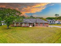 Charming single story brick home with a large lawn and mature tree, under a colorful sky at 3104 Umbrella Tree Dr, Edgewater, FL 32141