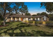 Charming single-story home featuring stone accents, a well-manicured lawn, and mature trees under a beautiful evening sky at 6247 Palomino Cir, Port Orange, FL 32127