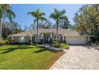 Charming home with a manicured lawn, brick driveway, and lush landscaping featuring palm trees at 6194 Half Moon Dr, Port Orange, FL 32127