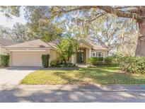 Charming single-story home featuring a manicured lawn, mature trees, and an inviting entrance, complete with a two-car garage at 32543 Crystal Breeze Ln, Leesburg, FL 34788