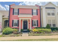 Charming two-story townhome featuring a bright pink facade, black shutters, and manicured landscaping at 103 Manor View Ln, Deland, FL 32724