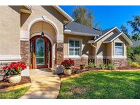 Charming home exterior featuring a stone accent, arched door and manicured front yard with vivid red poinsettias at 1309 Wicklow Ln, Ormond Beach, FL 32174