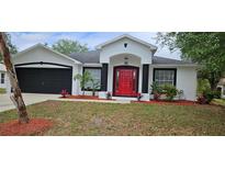 Charming single-story home with red door, black trim, fresh landscaping, and black two-car garage door at 1568 Pendleton St, Deltona, FL 32725