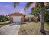 Charming brick home featuring a one-car garage, concrete driveway, and tropical landscaping at 2126 Sabal Palm Dr, Edgewater, FL 32141
