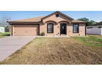 Tan single-story home with a two-car garage, brown roof, and tidy, drought-tolerant landscaping at 2448 Newmark Dr, Deltona, FL 32738