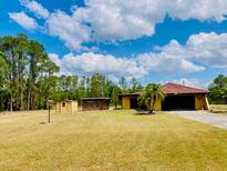Expansive front yard with a single-story home, wooden storage units, and a backdrop of lush trees at 7380 Orange Ave, Indian Lake Estates, FL 33855