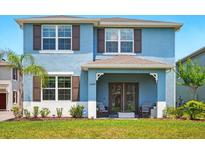 Charming two-story blue home featuring a covered front porch, lush landscaping, and beautiful architectural details at 3049 Meleto Blvd, New Smyrna Beach, FL 32168