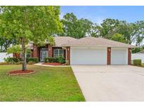 Charming brick home with a well-manicured lawn, mature trees, and a three car garage at 703 Elkhorn Fern Ln, Deland, FL 32720