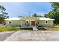 Charming single-story home featuring a covered porch, red doors, and manicured landscaping on a sunny day at 2953 Sled Rd, Christmas, FL 32709