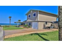 Beach home with a two-car garage, brick-paved driveway, grass lawn, and a covered outdoor entertainment area at 8 Ocean Dunes Dr, Ormond Beach, FL 32176