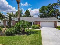 Charming brick home featuring a well-manicured lawn, mature trees, and an attached two-car garage at 832 Wildwood Cir, Port Orange, FL 32127