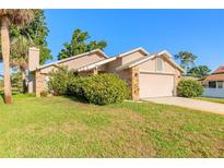 Charming tan home with a lush green lawn, mature trees, and a two-car garage at 929 N Lakewood Ter, Port Orange, FL 32127