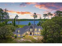 Stunning lakeside home with a stone exterior, manicured landscaping, and a tranquil water view at sunset at 5366 N Lake Farms Rd, De Leon Springs, FL 32130