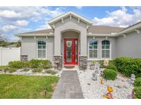 Charming home exterior featuring a decorative red front door and well-maintained landscaping at 413 Last Tree Dr, Deland, FL 32720