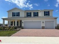 Two-story home with a two-car garage, red brick driveway, and manicured lawn under a clear blue sky at 3041 Cayey Way, Clermont, FL 34711