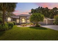 Charming home featuring a well-manicured lawn, lush landscaping, and a symmetrical facade enhanced by a colorful sunset sky at 8929 Sw 196Th Ct, Dunnellon, FL 34432
