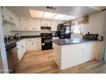 Bright kitchen featuring white cabinets, wood floors, black appliances, and a countertop bar at 6337 N 49Th Ave, Glendale, AZ 85301