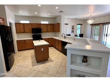 Bright kitchen features wood cabinetry, island, granite counters, black appliances, and breakfast bar with decorative shelving at 19661 N Echo Rim Dr, Surprise, AZ 85387