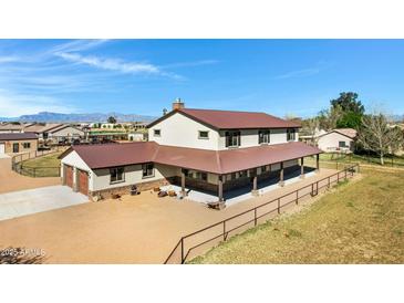 Expansive two-story home featuring a metal roof, large covered porch, and ample yard space under a bright blue sky at 4880 E Beehive Rd, San Tan Valley, AZ 85140