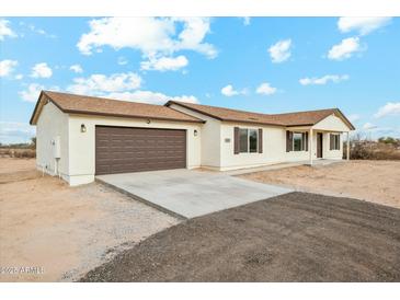 Inviting single-story home with neutral exterior, brown garage door, and well-lit entry showcases charm and curb appeal at 31812 N 221St Dr, Wittmann, AZ 85361