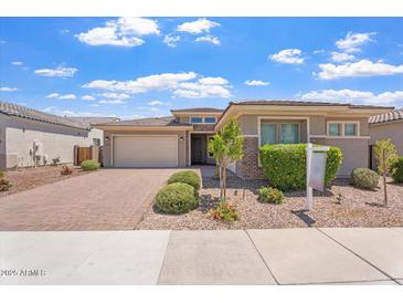Charming single-story home with a well-manicured front yard and a brick driveway, under a bright blue cloudy sky at 28389 N 131St Dr, Peoria, AZ 85383
