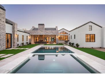 An elevated rear view of a backyard pool and stone patio surrounded by lush artificial lawn at 9810 N 57Th St, Paradise Valley, AZ 85253