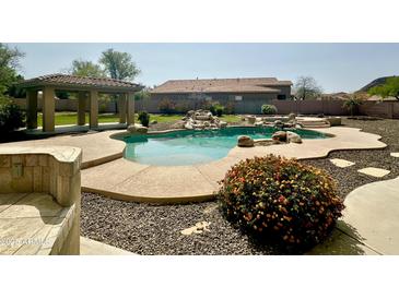 Backyard pool with rock waterfall feature, beautiful landscaping, and covered patio area at 9827 W Keyser Dr, Peoria, AZ 85383