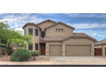 Tan two-story home with a three car garage, tile roof, desert landscaping, and secure window coverings at 43594 W Bravo Ct, Maricopa, AZ 85138