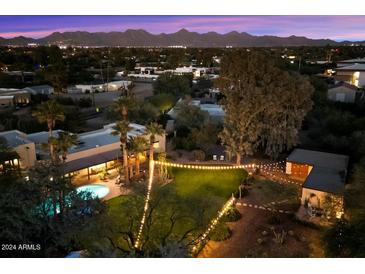 Aerial view of a stunning property with a pool, lush landscaping, and string lights at dusk at 6501 E Cholla St, Scottsdale, AZ 85254