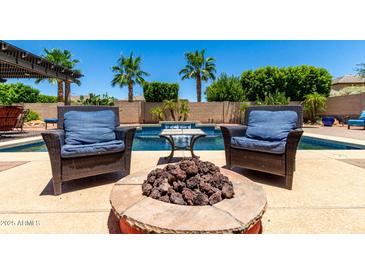 Inviting backyard oasis with a fire pit and comfortable seating by the refreshing pool and lush palm trees at 18174 W Wind Song Ave, Goodyear, AZ 85338