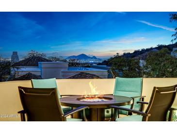 Evening view from a patio with fire pit, chairs, and city skyline in the background at 13503 E Charter Oak Dr, Scottsdale, AZ 85259