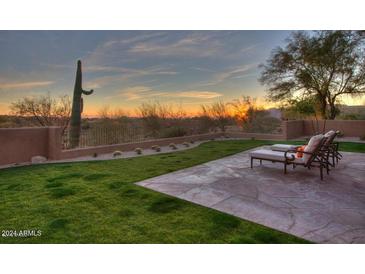 Sunset view from backyard patio with lounge chairs and grassy lawn at 9515 E Sundance Trl, Scottsdale, AZ 85262