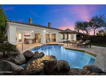 Backyard pool featuring a rock waterfall, lounge chairs, and covered patio area perfect for outdoor entertaining at 744 E County Down Dr, Chandler, AZ 85249