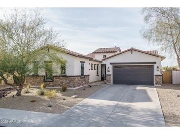 Charming home featuring a gray garage door, desert landscaping, and a mix of stone and stucco finishes at 15312 S 181St Dr, Goodyear, AZ 85338