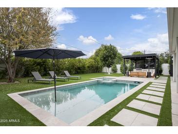 A backyard oasis featuring a pool, spa, outdoor kitchen, and lush landscaping, perfect for relaxation and entertaining at 329 E Belmont Ave, Phoenix, AZ 85020