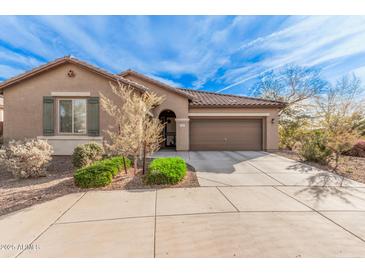 One-story house with tan exterior, landscaped yard, and two-car garage at 1727 N 213Th Dr, Buckeye, AZ 85396