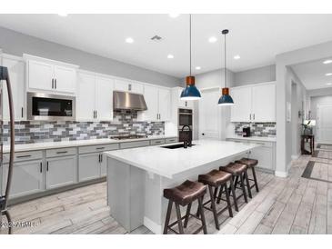 Modern kitchen featuring a large island, white cabinets, stylish backsplash, stainless steel appliances, and wood-look flooring at 20363 W Coolidge St, Buckeye, AZ 85396