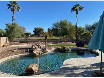 Inviting backyard oasis featuring a sparkling pool, waterfall, and lush landscaping at 11930 W Monroe St, Avondale, AZ 85323