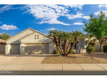 Tan two-car garage home with mature landscaping and a paved driveway at 18135 N Saddle Ridge Dr, Surprise, AZ 85374