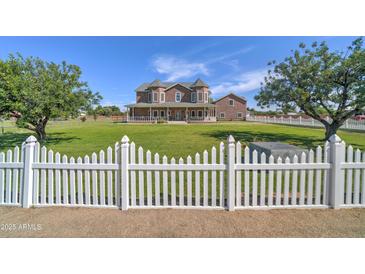 Charming two-story home features a well-maintained lawn, mature trees, and a classic white picket fence at 424 E Lehi Rd, Mesa, AZ 85203