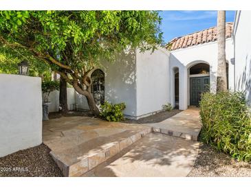 White stucco house with a tiled roof, featuring a stone walkway and lush landscaping at 8008 E Del Rubi Dr, Scottsdale, AZ 85258