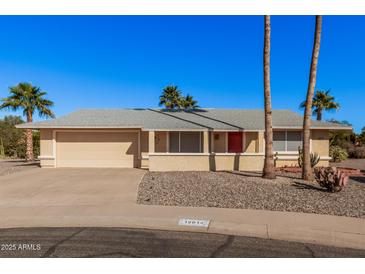 Tan one-story house with a red door, two-car garage, and desert landscaping at 18014 N Broken Bow Ct, Sun City, AZ 85373